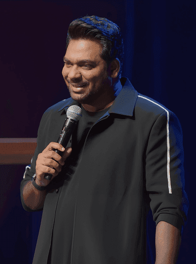 Zakir Khan on stage, arms open, before a packed hall
